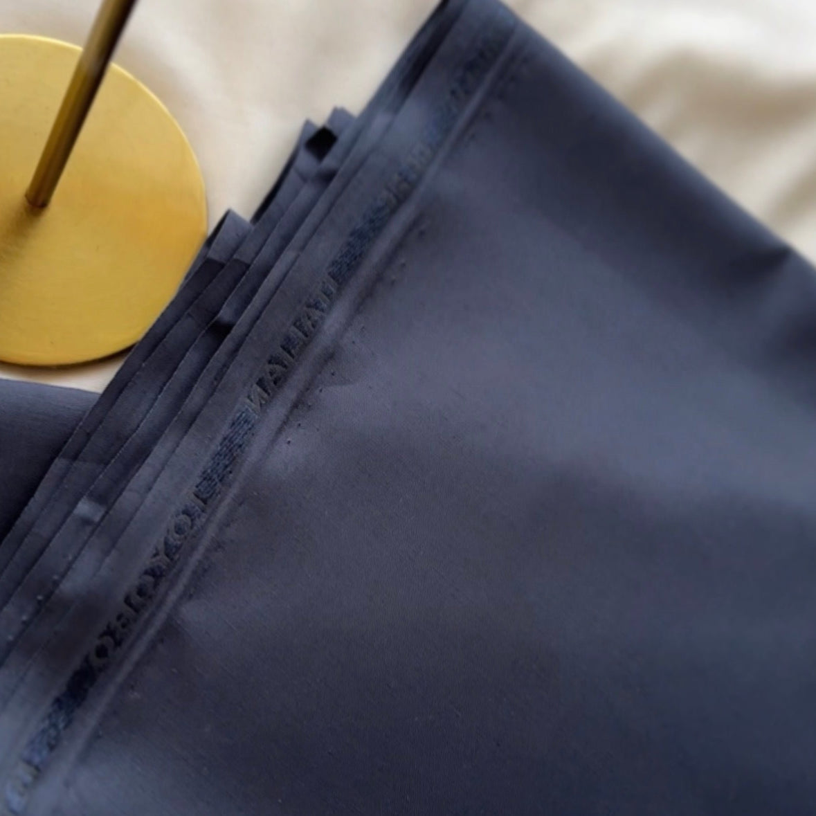 Close-up of a navy blue fabric with a gold circular object underneath